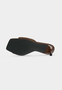 Chaussure marron à petit talon, couchée sur le côté montrant un bout carré et une semelle en caoutchouc noire avec un petit talon aiguille.