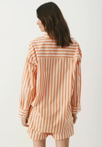 Oranžovo-bíle pruhovaná oversized košile s manžetami na knoflíky a detailem zadního sedla, spárovaná s odpovídajícími pruhovanými šortkami.
