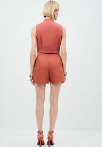 Rostfarbene, ärmellose Cropped-Top kombiniert mit passenden Shorts, aus einem strukturierten Stoff gefertigt, mit einem klaren, taillierten Design und schlichter Saumverarbeitung.