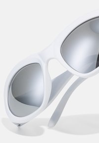 Ochelari de soare albaștri cu un finisaj mat, neted, având lentile gri ușor reflectorizante și un design unghiular, aerodinamic.