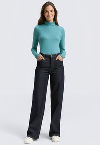 Turquoise long-sleeve turtleneck top paired with high-waisted dark blue wide-leg jeans. Smooth fabric with a fitted design and front pockets.