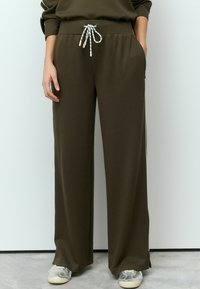 Olive green sweatpants with a drawstring waist, side pockets, and a relaxed fit. Made from soft fabric with a smooth texture.