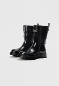 Bottes de cheville en caoutchouc noir avec un côté texturé, un logo en relief et une semelle crantée épaisse. La tige présente une finition brillante et des languettes de tirage.