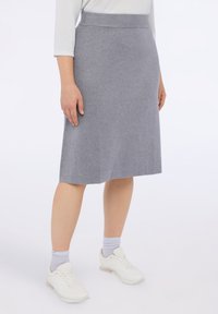 Harmaa neulehame, jossa on sileä pinta, polvipituinen muotoilu ja istuva vyötärö. Yhdistetty valkoisiin lenkkareihin ja vaaleanharmaisiin sukkiin.