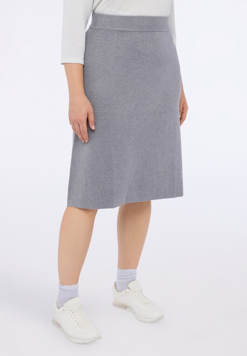 Harmaa neulehame, jossa on sileä pinta, polvipituinen muotoilu ja istuva vyötärö. Yhdistetty valkoisiin lenkkareihin ja vaaleanharmaisiin sukkiin.