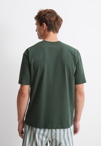 Grünes Kurzarm-T-Shirt aus weichem Stoff, mit klassischem Rundhalsausschnitt und lässiger Passform, von hinten gezeigt.