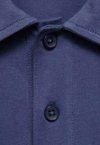Prim-plan al unui guler de cămașă polo de culoare bleumarin cu două nasturi negri, evidențiind textura țesăturii și detaliile cusăturii.