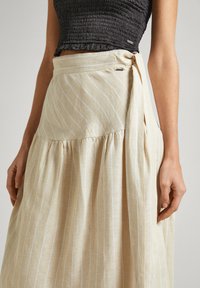 Valkoinentekoinen hame vaalean beige kankaan, jossa on valkoisia raitoja. Hameessa on kerroksellinen muotoilu ja sivusolki, joka korostaa tekstuurista ilmettä.