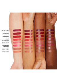Lipstick swatches on arms in various skin tones. Colors include grape soda, raspberry, cherry pie, and more. Smooth, glossy finish.