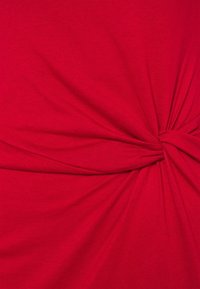 Röd trikåtyg med en vriden knutdetalj i mitten. Mjuk textur med lätt stretch. Jämn färg över hela tyget.