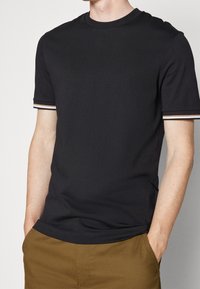 Zwart T-shirt met korte mouwen, een ronde hals en gestreepte details op de manchetten. Gemaakt van zachte stof en uitgevoerd in een klassieke pasvorm.