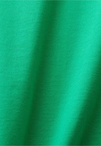 Gros plan d'un tissu vert lisse avec une texture de tissage visible et des ombres douces créant des plis subtils.