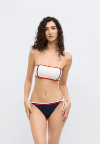 Μπικίνι τοπ χωρίς τιράντες σε κρεμ χρώμα με κόκκινες και ναυτικές λεπτομέρειες, και ταιριαστό μαγιό κάτω μέρος με κορδόνια στα πλαϊνά. Λεία υφή και εφαρμοστό σχέδιο.