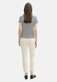 Camiseta a rayas en blanco y negro, de mangas cortas, combinada con pantalones ajustados de color crema y zapatos negros, vista desde la espalda.