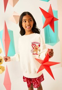 White sweatshirt with "Festive" graphic featuring a gingerbread man; red sequined skirt; surrounded by colorful geometric paper decorations.