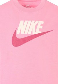 Camiseta de algodón rosa con un logo en blanco de "NIKE" y un gráfico de swoosh texturizado en rojo. Cuello redondo y mangas cortas.