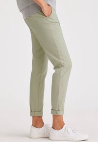 Ljusgröna tapered byxor i mjuktyg, med uppvikta fållar och sidofickor, i kombination med vita sneakers.