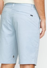 Light blue shorts made of smooth fabric, featuring a back pocket with a diagonal seam and a black logo tag near the hem.