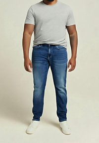 Miesten asu, joka koostuu vaaleanharmaasta lyhythihaisesta t-paidasta ja tummansinisistä kapeista farkuista haalistuneella pesulla, täydentyy valkoisilla tennareilla.