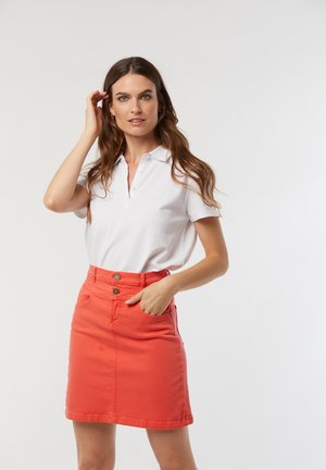 Un polo blanc associé à une jupe en denim corail. La jupe présente une taille haute, des poches avant et deux fermetures à boutons.