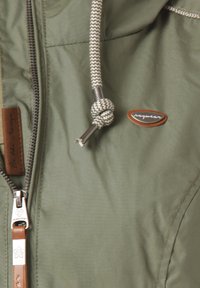 Giacca verde con chiusura a zip, tessuto testurizzato, coulisse in stile corda e un'etichetta in pelle marrone. Presenta un dettaglio con il logo del brand.