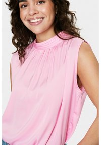 Blusa senza maniche rosa con scollo arricciato, tessuto leggero, texture liscia e taglio morbido, indossata da una persona che sorride.
