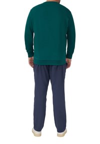 Zielona bluza z okrągłym dekoltem i dopasowanymi mankietami, zestawiona z granatowymi spodniami i jasnymi trampkami. Tekstura wydaje się miękka.