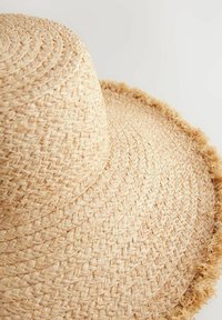 Sombrero de paja de ala ancha en color beige, con un patrón texturizado tejido y un borde deshilachado para mayor detalle.