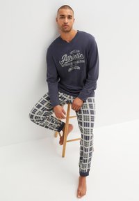 Maglietta a maniche lunghe blu navy con grafica "Athletic" e pantaloni da pigiama in plaid beige e blu navy, con polsini a coste e vestibilità rilassata.