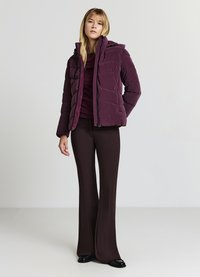 Giacca a vento bordeaux con chiusura frontale a zip, cappuccio e design trapuntato. Abbinata a pantaloni scuri a zampa e calzature nere.