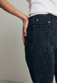 Jeans negre cu imprimeu de șarpe, confecționați din denim, având talie medie, design cu cinci buzunare și detalii din metal argintiu.
