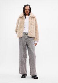 Faux fur-beige jakke med bred krage, kombinert med høytlivede grå rette jeans. Svart kraftige støvler, langt fletet hår.