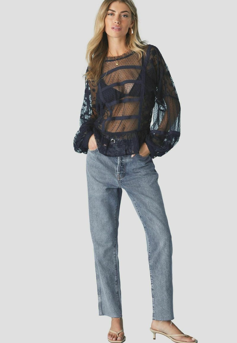 Haut transparent bleu marine à motif pois et manches bouffantes, associé à un jean taille haute bleu clair et des sandales beiges.