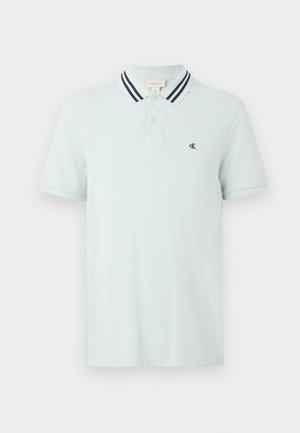 Svijetloplava polo majica kratkih rukava s tamnoplavim prugama na ovratniku, placket-om s dva dugmeta i malim tamnim "CK" logo-om na lijevoj strani prsnog koša.