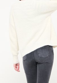 Vit, fluffig stickad tröja med en lös passform, kombinerad med mörkgrå, figurnära jeans med femfickdesign.