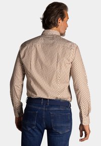Overhemd met lange mouwen en knopen, met een beige basis en kleine bruine stippen. Gecombineerd met donkerblauwe denim jeans en een gevlochten riem.
