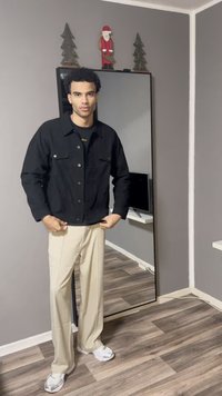 Jachetă din denim negru cu nasturi argintii, asortată cu pantaloni largi de culoare crem și adidași albi, într-o cameră cu o oglindă și decorațiuni.