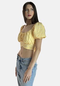 Top corto giallo a quadri con maniche a sbuffo, scollo quadrato e corpino arricciato. Abbinato a jeans azzurri a vita alta.