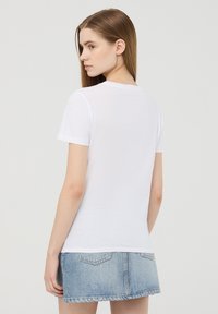 T-shirt bianco a maniche corte con scollatura rotonda, texture liscia e design aderente, abbinato a una gonna di jeans azzurra.