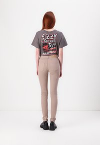 T-shirt graphique gris avec des motifs rouges et noirs au dos, associé à un jean beige ajusté et des chaussures noires.