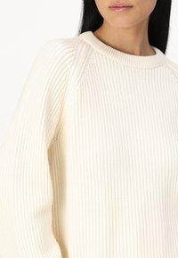 Pull crème côtelé avec un col rond et des manches raglan, fabriqué dans un tissu doux avec une finition texturée.