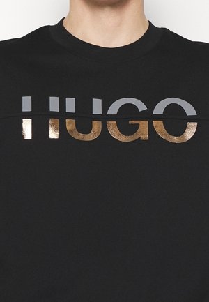 Czarna bluza z napisem "HUGO" w pogrubionych, metalicznych złotych i szarych literach. Gładka tkanina z okrągłym dekoltem i minimalistycznym wzornictwem.