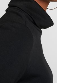 Maglione a collo alto nero realizzato in materiale morbido e elasticizzato con un design aderente. Presenta un colletto alto e una texture liscia.