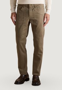 Pantalones de sarga de algodón marrón con corte recto, bolsillos frontales, costura decorativa y cierre con botón en la parte delantera, combinados con zapatos marrones oscuros.