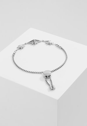 Zilveren verstelbare armband met stervormige bedels en een centrale schuifsluiting, weergegeven op een wit geometrisch platform.