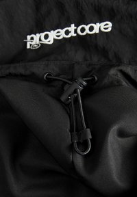 Intérieur en nylon noir avec fermeture à cordon. Présente une broderie "project core" en blanc et une texture lisse avec un léger éclat.