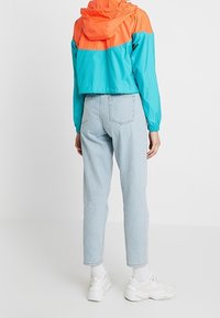 Beskurad vindjacka med orange och teal färgblock, hög krage och elastiska ärmar. Matchad med ljusblå jeans och vita sneakers.