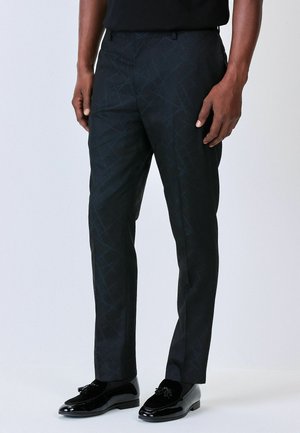 Schwarze gemusterte Hose mit geometrischem Design, schlanker Schnitt und tailliertem Schnitt. Getragen mit glänzenden schwarzen Mokassins.