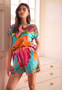 Costum din bumbac în culori vii, cu un model floral în nuanțe de portocaliu, roz și verde. Designul include mâneci scurte și talie elastică.