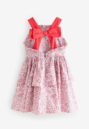 Vestido floral con un patrón en rosa y blanco, acentos de lazo rojo en los tirantes, cintura fruncida y falda de volantes en capas.